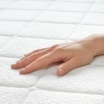 Choosing mattress and bed. Close-up of female hand touching and testing mattress in a store. Copy space.